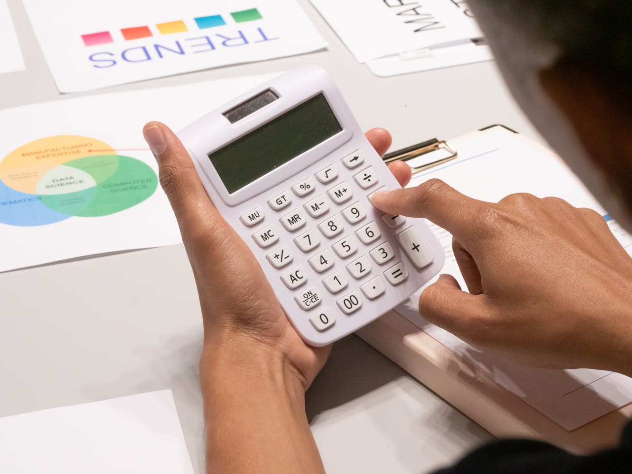 Close-up of a person's hand using a calculator on a desk with financial documents.